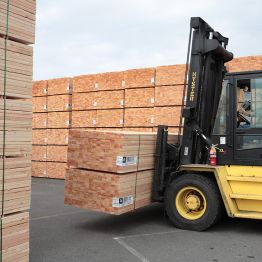 Image of a forklift carring two stacks of lumber while surrounded by tall stacks of lumber.